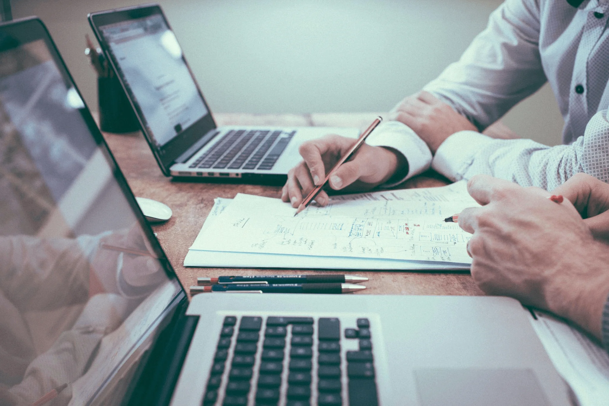 A person holding a pencil and reviewing notes near a laptop, symbolizing the assessment of content marketing metrics for content quality and effectiveness.